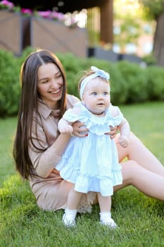 Young happy woman sitting on grass with little female baby. Concept of motherhood and children, resting on open air.