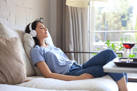 Beautiful brunette woman in earphones sitting on sofa listening to music with closed eyes