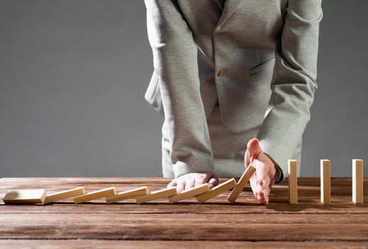 Close up female hand interrupting domino effect. Operative business solution, strategy and successful intervention. Business assistance concept with wooden blocks. Protection from economic crisis.