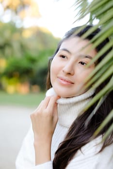 Portrait of korean woman wearing white sweater standing near palm leaf. Concept of asian beauty and female person.