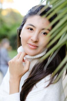 Portrait of japanese woman wearing white sweater standing near palm leaf. Concept of asian beauty and female person.