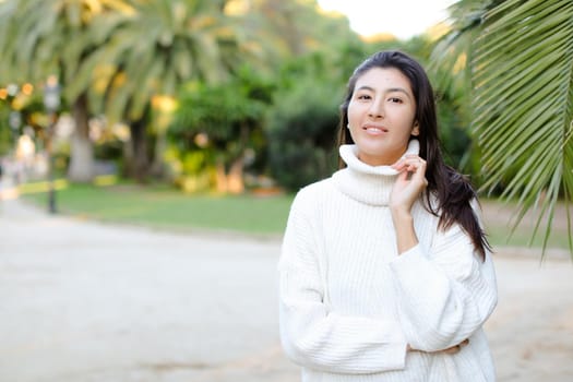 Korean woman in white sweater standing near palm leaf. Concept of asian beauty and female person on tropical resort.