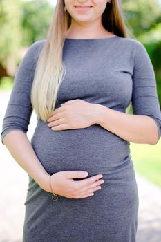 Young pregnant girl wearing grey dress holding belly. Concept of expectant female person and motherhood.