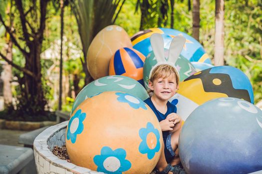 Cute little kid boy with bunny ears having fun with traditional Easter eggs hunt, outdoors. Celebrating Easter holiday. Toddler finding, colorful eggs.