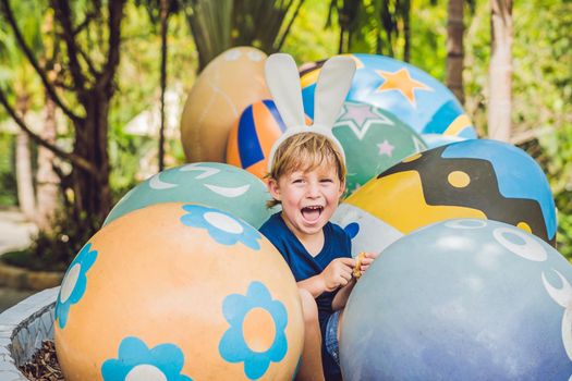 Cute little kid boy with bunny ears having fun with traditional Easter eggs hunt, outdoors. Celebrating Easter holiday. Toddler finding, colorful eggs.