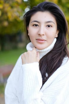 Portrait of asian woman wearing white sweater walking in autumn park. Concept of chinese girl.