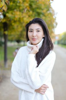 Asian nice woman wearing white sweater walking in autumn park. Concept of chinese girl.