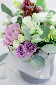 Closeup wedding bouquet with rings, white wall background. Concept of floristic art and bridal thigs.