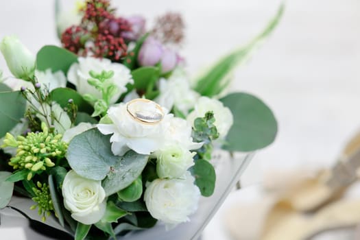 Closeup wedding nice bouquet with rings, white wall background. Concept of floristic art and bridal thigs.