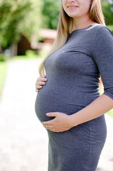 Young pregnant blonde girl wearing grey dress holding belly. Concept of expectant female person and motherhood.