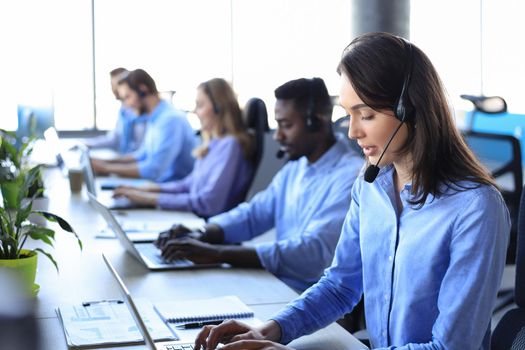 Female customer support operator with headset and smiling, with collegues at background