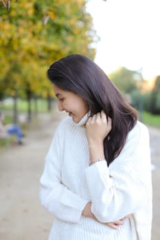 Asian woman wearing white sweater walking in autumn park. Concept of chinese girl.