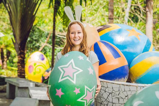 Beautiful young woman with bunny ears having fun with traditional Easter eggs hunt, outdoors. Celebrating Easter holiday.