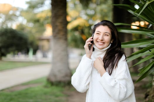 Japanese happy girl in tropical park talking by smartphone near palm. Concept of modern techology and nature.