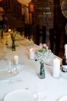 Bouguet of flowers, white plates with forks and candles on table. oncept of romantic dinner and catering establishment.