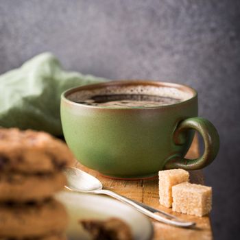 Cup of coffee with chocolate chip cookies on green plate on old wooden table. Selective focus.