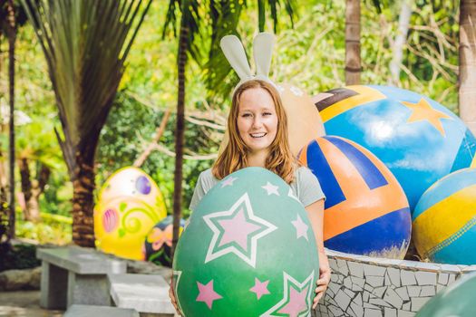 Beautiful young woman with bunny ears having fun with traditional Easter eggs hunt, outdoors. Celebrating Easter holiday.