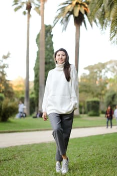 Asian stylish woman walking in tropical park and wearing white sweater. Concept of nature and female person.