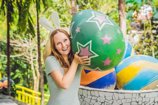 Beautiful young woman with bunny ears having fun with traditional Easter eggs hunt, outdoors. Celebrating Easter holiday.