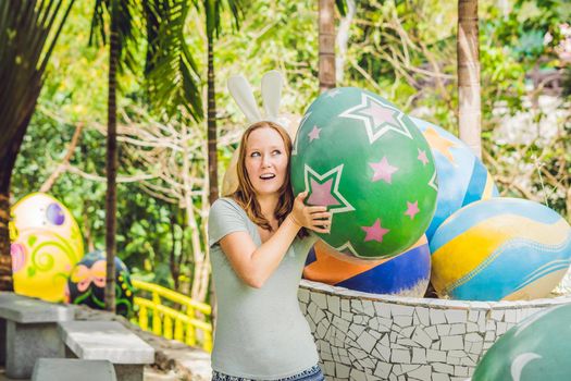 Beautiful young woman with bunny ears having fun with traditional Easter eggs hunt, outdoors. Celebrating Easter holiday.