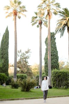 Chinese cute girl walking in tropical park and wearing white sweater. Concept of asian beauty and nature.