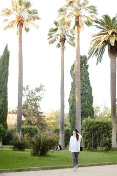 Chinese girl walking in tropical park and wearing white sweater. Concept of asian beauty and nature.