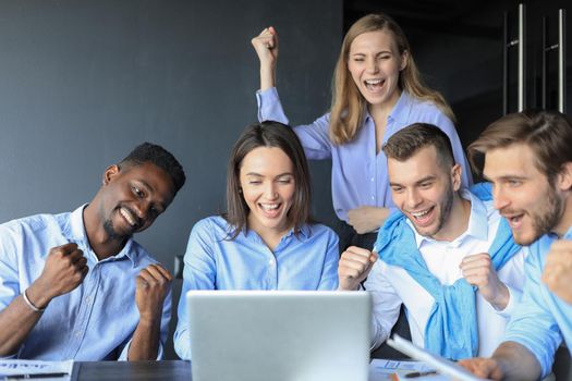 Happy business people laugh near laptop in the office. Successful team coworkers joke and have fun together at work.