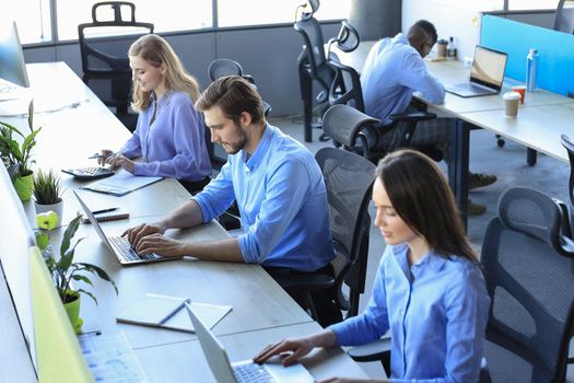 Office routine. Group of young business people in smart casual wear working and communicating while sitting at desk in the office