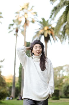 Korean cute woman walking in tropical park and wearing white sweater. Concept of nature and female person.