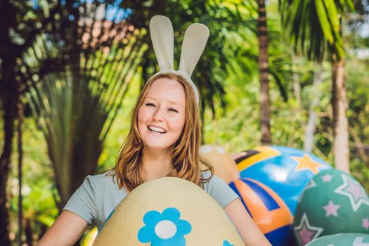 Beautiful young woman with bunny ears having fun with traditional Easter eggs hunt, outdoors. Celebrating Easter holiday.