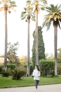 Chinese nice girl walking in tropical park and wearing white sweater. Concept of asian beauty and nature.