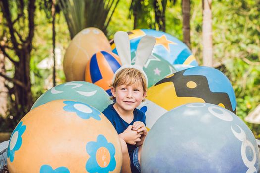 Cute little kid boy with bunny ears having fun with traditional Easter eggs hunt, outdoors. Celebrating Easter holiday. Toddler finding, colorful eggs.