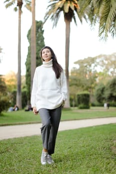 Asian nice woman walking in tropical park and wearing white sweater. Concept of nature and female person.
