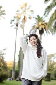 Korean beautiful woman walking in tropical park and wearing white sweater. Concept of nature and female person.