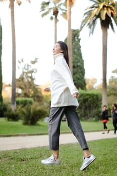 Asian woman walking in tropical park and wearing white sweater. Concept of nature and female person.