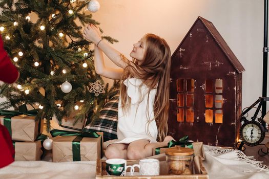 Excited girl smiling while sitting on a carpet and putting decorations on Christmas tree