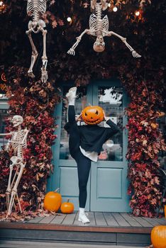Girl with a pumpkin head posing at the door on the street . Halloween Concept