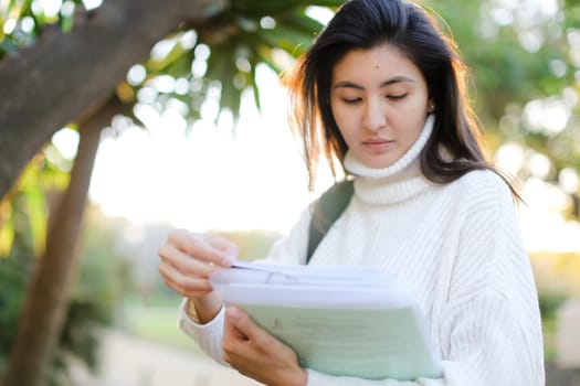 Focus on chinese girl keeping documents and walking outdoors. Concept of asian student.