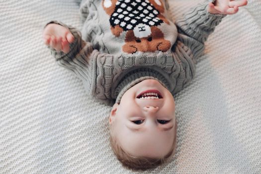 Upside down photo of an adorable toddler on warm sweater laying on bed and laughing