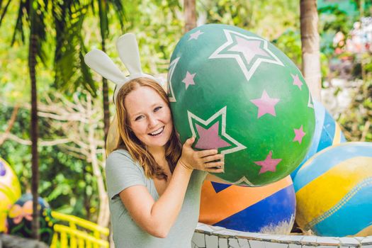 Beautiful young woman with bunny ears having fun with traditional Easter eggs hunt, outdoors. Celebrating Easter holiday.