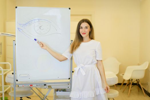 Female cosmetologist draws eye on placard at cosmetology cabinet. Concept of permanent makeup courses and beauty salon.