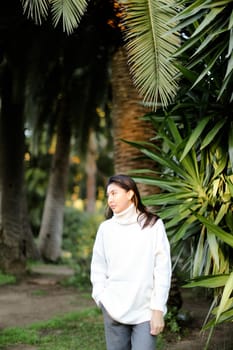 Chinese girl walking in tropical park and standing near palms. Concept asian beauty and nature.