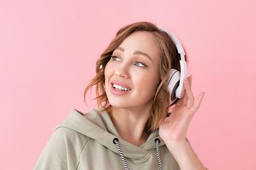 Happy teeth smile woman listen music headphones Caucasian female enjoy podcast or audio books dressed oversize hoodie pink background close up portrait