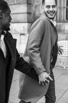 Black and white bw portrait in Paris. Caucasian man running with afroamerican male person and holding hands in city. Concept of happy gays and strolling.