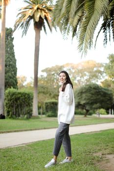 Chinese beautiful girl walking in tropical park and wearing white sweater. Concept of asian beauty and nature.