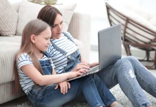 mom and daughter sitting on the carpet in the living room and using a laptop.photo with copy space