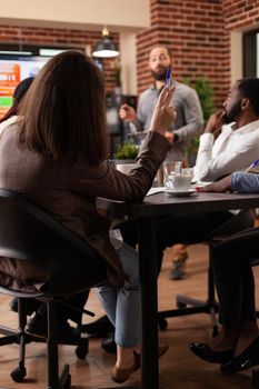 Multi-ethnic businessteam working at marketing presentation analyzing company graphs working in startup office. Businesswoman rising hand having business question for partnership project