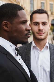 close up portrait of same sex couple. caucasian man wearing suit standing near afro american boy. Concept of business and male fashion.