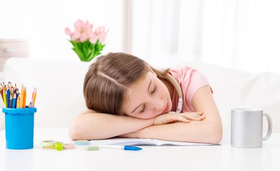 Cute lovely schoolgirl is tired and sleeps on desk indoors