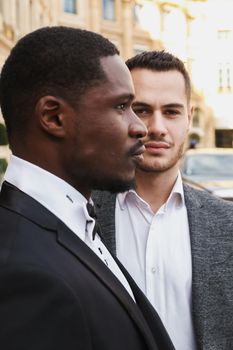 close up portrait of same sex couple. caucasian man wearing suit standing near afro american boy. Concept of business and male fashion.